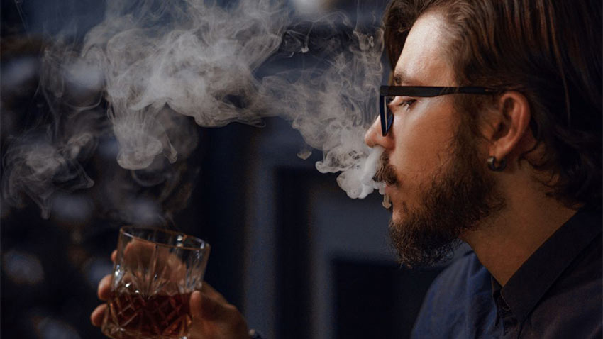 barbat care fumeaza si are un pahar cu bautura alcoolica in mana