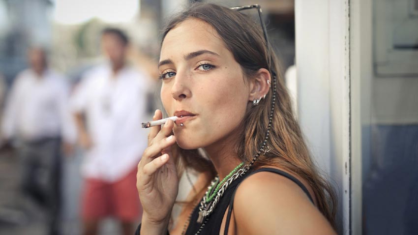 Femeie care fumeaza o tigara rulata cu persoane in fundal