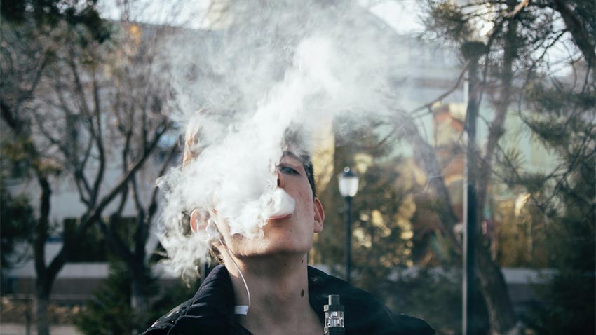 baiat care fumeaza tigara electronica intr-un parc