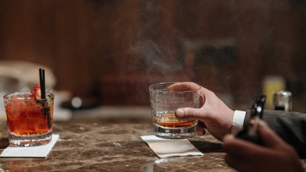 barbat care fumeaza la un pahar de bautura impreuna cu cineva