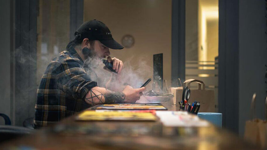 barbat stand la o masa si fumand dintr-o tigara electronica