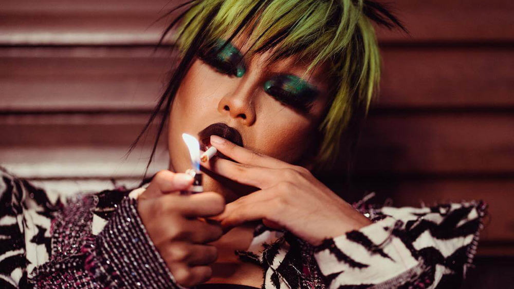 femeie cu par verde imbracata elegant care fumeaza o tigara