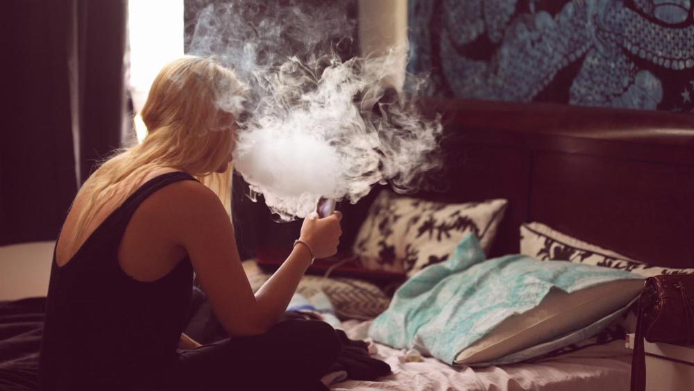 femeie care fumeaza o tigara electronica in pat