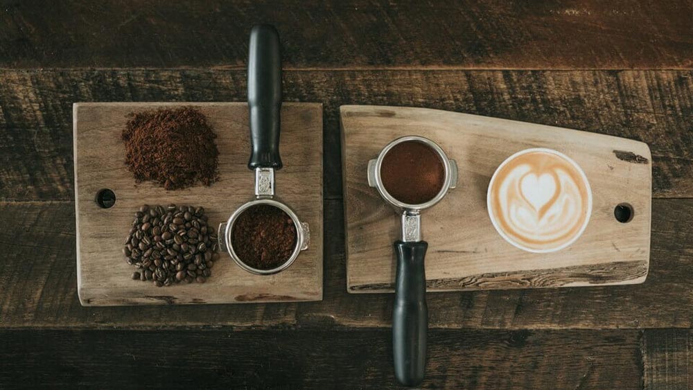 ceasca de cafea langa 2 portafiltre de cafea pe o masa din lemn