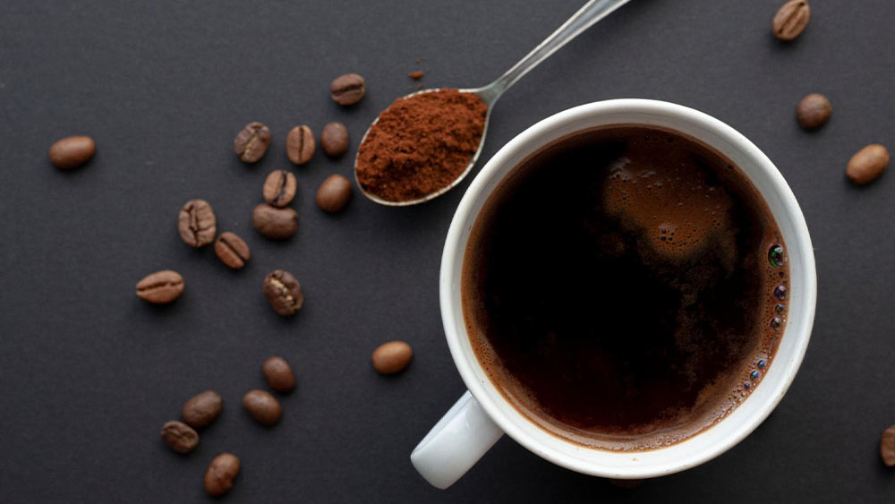 ceasca de cafea pe masa cu o lingura de cafea macinata si boabe