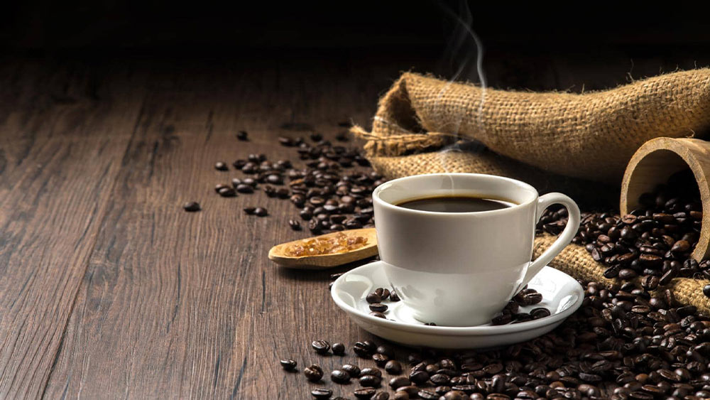cana de cafea pe o masa inconjurata de boabe de cafea