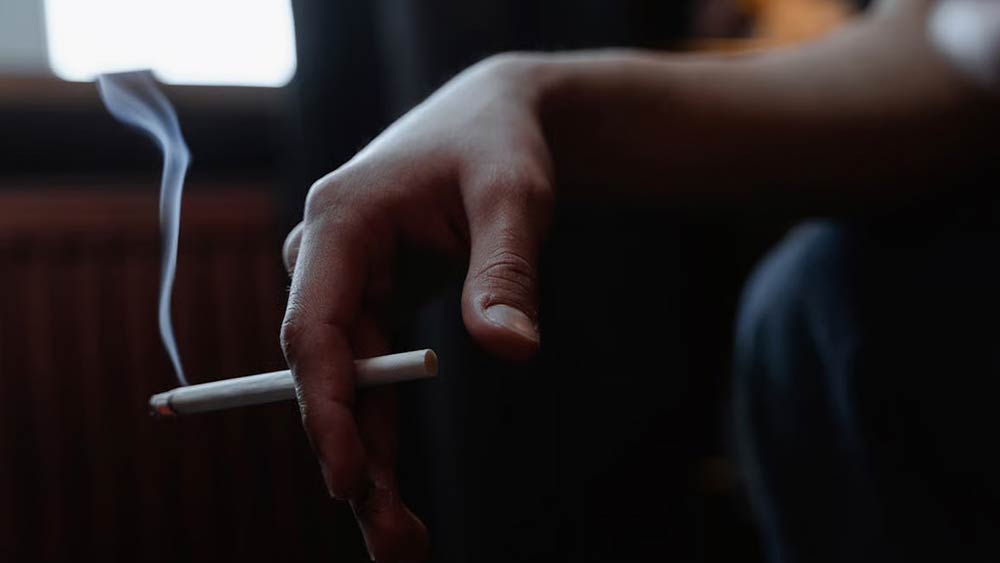Persoana care tine in mana o tigara rulata aprinsa