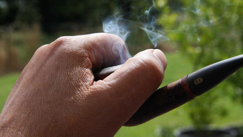 Barbat care tine o pipa de fumat aprinsa in mana