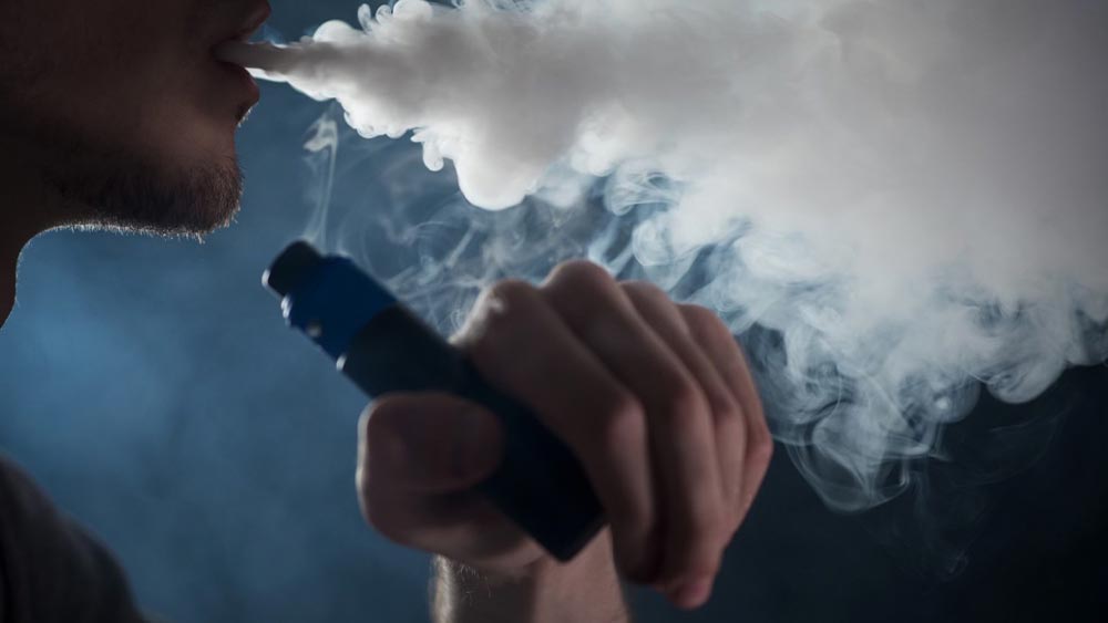 Barbat care vapeaza si sufla un nor de fum