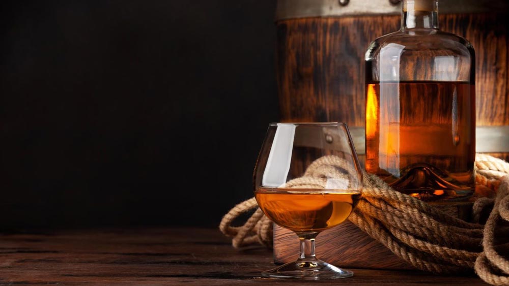 Pahar si sticla de coniac langa o funie si un butoi din lemn