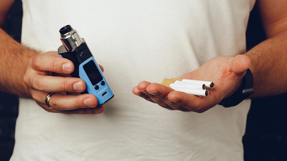 Barbat care tine in maini un vape si mai multe tigari