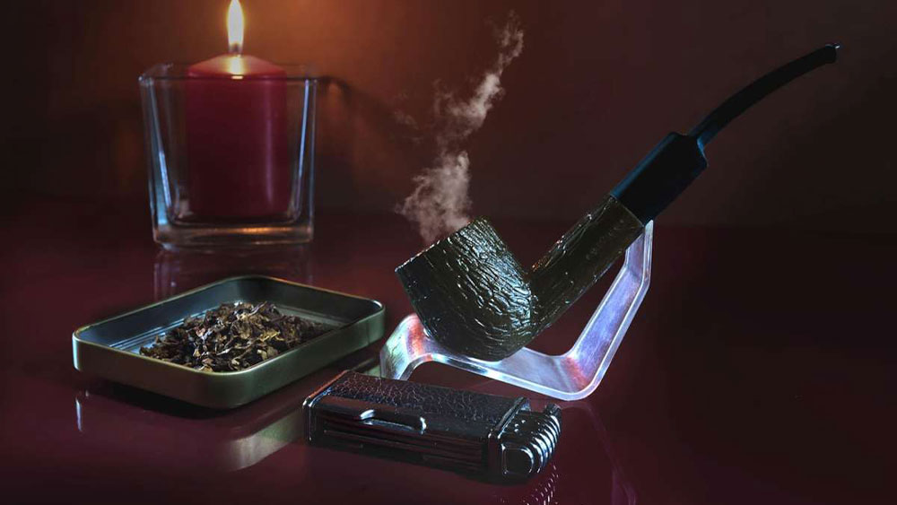 O pipa de fumat in suport langa tutun si bricheta de pipa