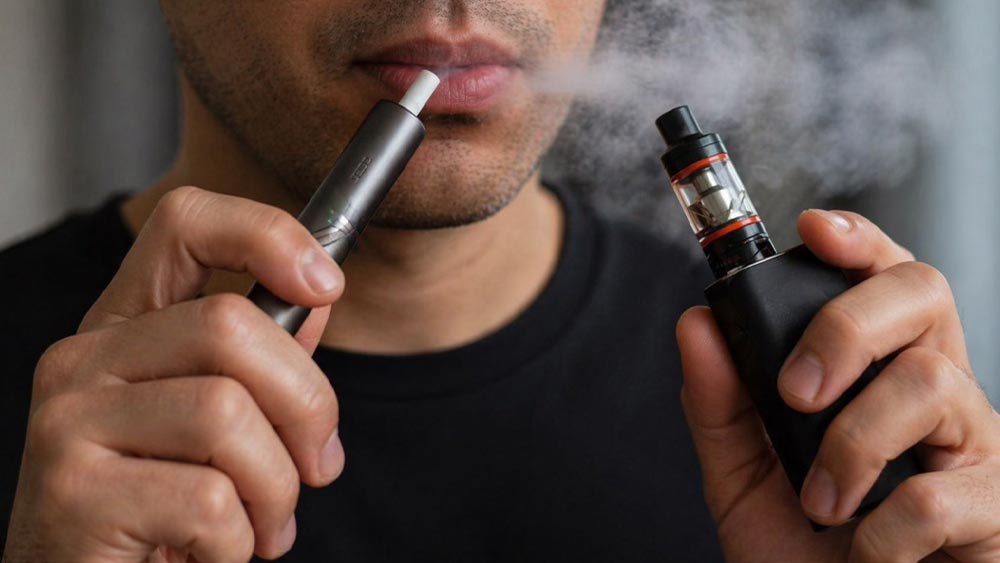 Barbat care fumeaza din vape si dintr-un aparat de incalzit tutun