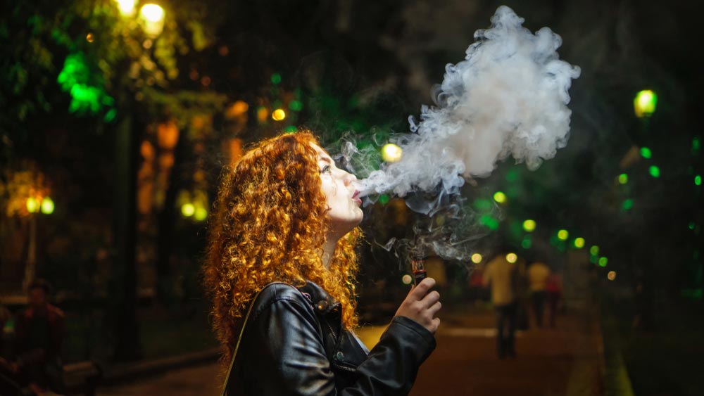 Fata care fumeaza tigara electronica si sufla un nor de fum
