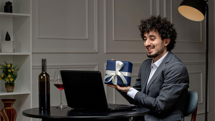 barbat cu un cadou prezentat la laptop langa vin